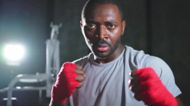 Spor salonunda boksör. Saldırgan Afrikalı dövüşçü boks eğitiminden sonra dinleniyor kameraya bakarak dövüşmeye hazır. Güçlü terli adam yumruklarını eğitiyor. Doğruca antrenmana hazırlanıyor.