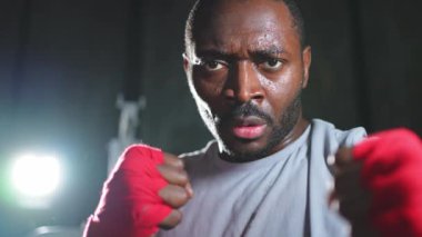 Spor salonunda boksör. Saldırgan Afrikalı dövüşçü boks eğitiminden sonra dinleniyor kameraya bakarak dövüşmeye hazır. Güçlü terli adam yumruklarını eğitiyor. Doğruca antrenmana hazırlanıyor.
