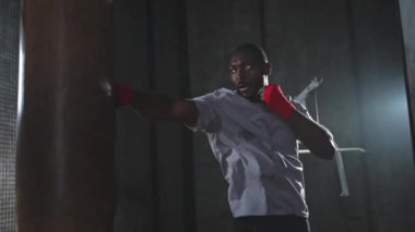 Beden eğitiminde spor. Güçlü Afrikalı dövüşçü boks torbasıyla yumruk eğitimi veriyor. Spor salonunda boks torbası yumruklayan sağlıklı bir boksör. Boks salonunda antrenman günü. Vücut çalıştırma eğitimine uygun güç