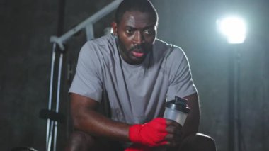 Spor salonunda boksör. Spor salonundaki boks antrenmanından sonra dinlenen kırmızı boks ambalajlı yorgun Afrikalı boksör. Boks müsabakasından sonra güçlü, terli bir sporcu. Spor salonunda antrenman günü