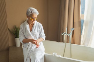 Olgun, yaşlı bir kadın ellerinde nemlendirici vücut losyonu sürüyor. Son sınıf öğrencisi kadın banyoda günlük cilt bakımını yaparken anti-yaş kremi sürüyor. Güzellik tedavisi vücut bakımını kapsar.