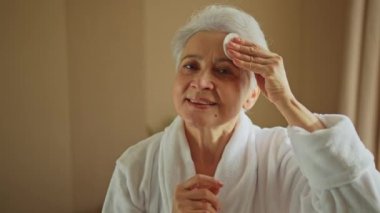 Yetişkin, yaşlı bir kadın günlük güzellik rutini yapıyor pamukla makyaj yapıyor. Losyon süngerli yaşlı kadın yüz bakımı yaptırıyor. Cilt bakımı yaşlandırıcı cilt temizleyici