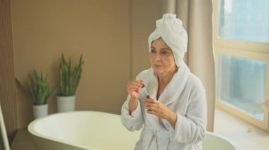 Cilde doğal damla kozmetik yağı süren bir kadın. Yetişkin yaşlı bir kadın günlük güzellik rutini yapan pipetli anti-yaş serumu uyguluyor. Yaşlı kadın yüz bakımı yaptırıyor.