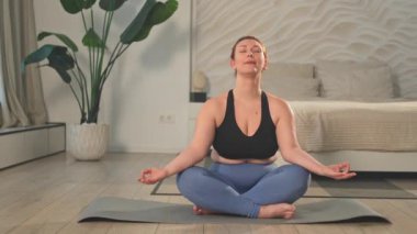 Yoga farkındalığı meditasyonu. Evde yoga yapan bir kadın. Artı nilüfer çiçeğinin üzerinde oturan kadın meditasyon yapıyor içeride rahatlarken gülümsüyor. Nefes egzersizi yapan bir kız. Evde yoga.