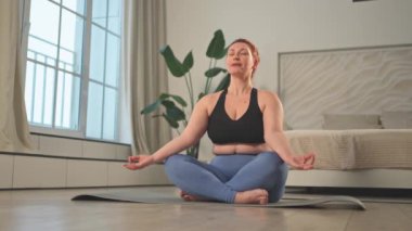 Yoga farkındalığı meditasyonu. Evde yoga yapan bir kadın. Artı nilüfer çiçeğinin üzerinde oturan kadın meditasyon yapıyor içeride rahatlarken gülümsüyor. Nefes egzersizi yapan bir kız. Evde yoga.