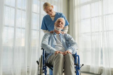 Emeklilik sağlık hizmetlerine destek ol. Hemşire tekerlekli sandalyedeki yaşlı adama yardım ediyor. Hasta ve kadın tıbbi bakım için huzurevinde. Engelli insanlar için tekerlekli sandalyede felçli bir adama bakan hemşire.