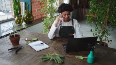 Afrikalı çiçekçi kadın bahçıvan botanik mağazasında çalışıyor. Müşteriyle telefon görüşmesi yaparak dizüstü bilgisayar siparişleri veren bitkiler kullanıyor. Çiçekçide çalışan küçük bir kadın işyeri sahibi. Kendi işini kur.