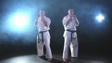 Karanlık arka planda dövüş sanatları ustaları. Siyah spor salonunda karate dövüş sporları eğitimi için beyaz kimonolu güçlü dövüşçüler. Karate dövüşçüleri antrenman yapıyor. Dövüş antrenmanı yapıyor.