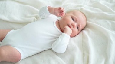 Mutlu bebek. Yatak odasında, gülümseyen yüzüyle küçük şirin bir kız. Bebek dinleniyor, evde beyaz battaniyeye uzanmış oynuyor. Annelik mutlu çocuk bakımı konsepti