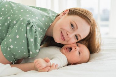 Evde mutlu bir aile. Anne, küçük bebekle yatakta oynuyor. Anne bebek birlikte oynayıp rahatlıyor. Annem kameraya sevgiyle bakar. Bebeği emziren anne oturma odasında dinleniyor.