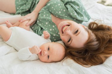 Evde mutlu bir aile. Anne, küçük bebekle yatakta oynuyor. Anne bebek birlikte oynayıp rahatlıyor. Annem kameraya sevgiyle bakar. Bebeği emziren anne oturma odasında dinleniyor.