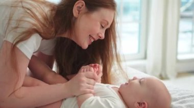 Evde mutlu bir aile. Anne, küçük bebekle yatakta oynuyor. Anne bebek birlikte oynayıp rahatlıyor. Anne bebeğe sevgiyle bakar. Bebeği emziren anne oturma odasında dinleniyor.