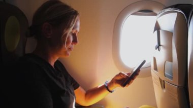 Yolcu kadın uçakla geliyor. Uçak penceresinin yanında oturan telefonu kullanan bir kız. Uçuşun tadını çıkaran akıllı telefonlu gezgin bir kadın. Gemide kablosuz bağlantı kullanan bir kadın var. Gezgin kız.