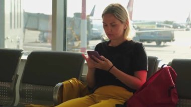 Havaalanı terminali. Akıllı telefon kullanan bir kadın uçuşu bekliyor. Havaalanında cep telefonlu bir kız internet sosyal medya uygulamalarında sörf yapıyor. Havayolu merkezinin pansiyonunda seyahat eden bir kadın. Gezgin kız.