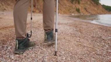 Turizm macerası yürüyüşü. Göl kenarında sırt çantalı, tanınmayan yürüyüşçü kız turist. Sırt çantalı kadın ayakları ve güzel sahil manzarası. Arkaya bakan kadın aktif turizm gezisinin tadını çıkarıyor