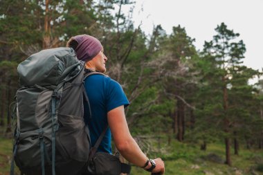 Turizm macerası yürüyüşü. Gezgin adam güzel manzaraya bakıyor. Yeşil ormanda gezen sırt çantalı bir turist. Arkaya bakan adam aktif turizm gezisinin tadını çıkarıyor