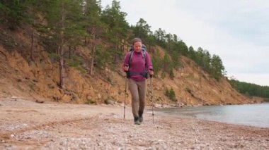 Turizm macerası yürüyüşü. Sırt çantalı gezgin bayan turist göl kenarında yürüyor. Gezgin kadın güzel sahil manzarasını seyrediyor. Genç ve mutlu bir kadın aktif turizm gezintisinin tadını çıkarıyor.