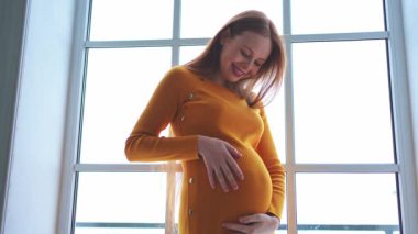 Hamilelik anneliği insanların gelecek beklentisi. Evinin penceresinin yanında koca göbekli hamile bir kadın var. Karnına sarılan ve hamileliğin tadını çıkaran bir kız. Annelik şefkati ebeveynlik yeni yaşam konsepti