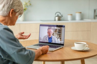 Kıdemli doktor uzman, yaşlı bir kadını internetten inceliyor. Yaşlı kadın hasta ve doktor görüntülü telefonda dizüstü bilgisayarla görüşüyor. Tıbbi sağlık hizmetleri sağlık kontrolü. Online doktor.