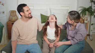 Evde mutlu bir aile. Anne, baba, kız, kanepede uzanıyor. Anne baba ve küçük kız sarılıp eğlenerek rahatlıyor. Gülümseyen aile, şefkatli anların tadını çıkarıyor