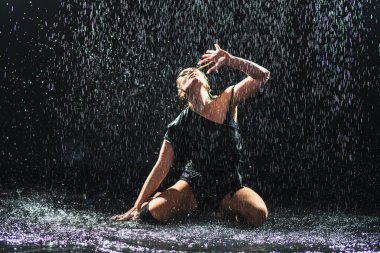 Siyah arka planda yağmur suyunda poz veren çağdaş kadın dansçı. Dişi sanatçı ifade ile dans ediyor. Modern balerin karanlıkta dans ediyor. Tutku karanlıkta dans eder. Esneklik dengesi