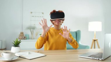 Evde sanal gerçeklik metavers VR gözlüğü takan Afro-Amerikalı genç bir kadın. Sanal gerçeklik kaskındaki sanal gerçeklik deneyimi sırasında havaya dokunan kız. Yüksek teknolojili simülasyon video oyunu kavramı