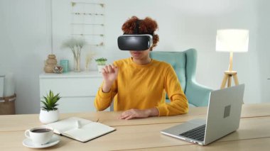 Evde sanal gerçeklik metavers VR gözlüğü takan Afro-Amerikalı genç bir kadın. Sanal gerçeklik kaskındaki sanal gerçeklik deneyimi sırasında havaya dokunan kız. Yüksek teknolojili simülasyon video oyunu kavramı