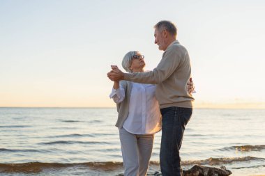 Yürümeye devam. Romantik olgun çift plaj gezisinde birlikte dans ediyor. Mutlu gülümseyen aile emeklisi kadın koca eş birlikte eğleniyor. Aile zamanı aşk bakımı