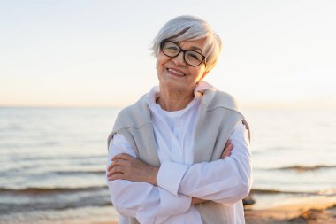 Kendine güveni tam orta yaşlı, orta yaşlı bir kadının açık hava portresi. Yaşlı olgun bir bayan sahilde gülümsüyor. Mutlu, çekici, son sınıf öğrencisi, kamera görüntüsü, yüz portresi. Mutlu insanlar.