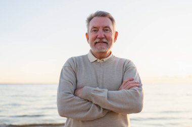 Sahilde kendine güveni tam orta yaşlı bir Avrupalı 'nın açık hava portresi. Yaşlı, olgun bir adam gülümsüyor. Mutlu büyükbaba kameraya bakıyor. Yüz portresi yakın çekim. Mutlu insanlar.