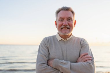 Sahilde kendine güveni tam orta yaşlı bir Avrupalı 'nın açık hava portresi. Yaşlı, olgun bir adam gülümsüyor. Mutlu büyükbaba kameraya bakıyor. Yüz portresi yakın çekim. Mutlu insanlar.