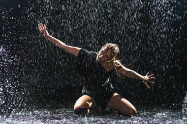 Siyah arka planda yağmur suyunda poz veren çağdaş kadın dansçı. Dişi sanatçı ifade ile dans ediyor. Modern balerin karanlıkta dans ediyor. Tutku karanlıkta dans eder. Esneklik dengesi