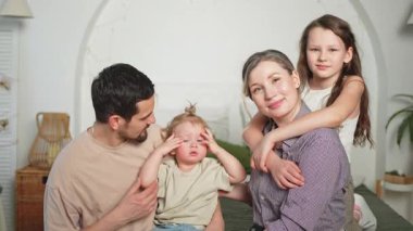 Evde mutlu bir aile. Anne baba, iki kız evlat kanepede dinleniyorlar. Anne, baba, anne, baba, kız, çocuklar birlikte oynayıp rahatlıyorlar. Gülümseyen aile, şefkatli anların tadını çıkarıyor