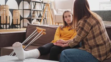 Kırık bacağı alçıda olan bir kız evde kanepede annesiyle oturuyor. Kırık bacağı iyileşen üzgün genç bir çocuk. Hızlı rehabilitasyon için koltuk değneklerini kullanan bir kız. Anne destek kızı