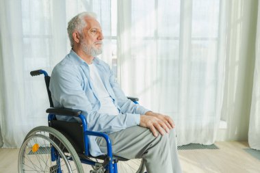 Tekerlekli sandalyede oturan üzgün yaşlı adam huzurevinin penceresinden dışarı bakıyor. Engelli insanlar için tekerlekli sandalyedeki yaşlı felçli adam depresyonda. Yalnız yaşlı hasta adam tekerlekli sandalyede oturuyor.