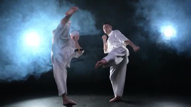 Karanlık arka planda dövüş sanatları ustaları. Siyah spor salonunda karate dövüş sporları eğitimi için beyaz kimonolu güçlü dövüşçüler. Karate dövüşçüleri antrenman yapıyor. Dövüş antrenmanı yapıyor.