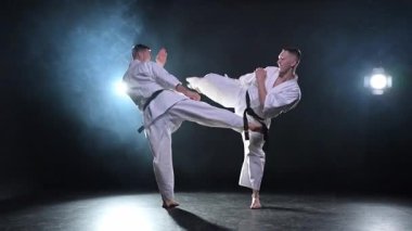 Karanlık arka planda dövüş sanatları ustaları. Siyah spor salonunda karate dövüş sporları eğitimi için beyaz kimonolu güçlü dövüşçüler. Karate dövüşçüleri antrenman yapıyor. Dövüş antrenmanı yapıyor.