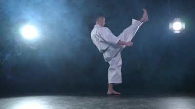 Siyah kuşaklı karate dövüş sanatları için beyaz kimonolu güçlü adam siyah arka plandaki dövüş eğitimine hazırlanıyor. Antrenman hareketleri yumruklar gölge dövüşü alıştırmaları antrenmana hazır.