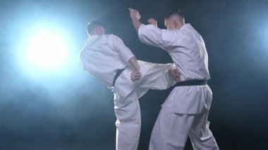 Karanlık arka planda dövüş sanatları ustaları. Siyah spor salonunda karate dövüş sporları eğitimi için beyaz kimonolu güçlü dövüşçüler. Karate dövüşçüleri antrenman yapıyor. Dövüş antrenmanı yapıyor.