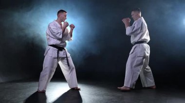 Karanlık arka planda dövüş sanatları ustaları. Siyah spor salonunda karate dövüş sporları eğitimi için beyaz kimonolu güçlü dövüşçüler. Karate dövüşçüleri antrenman yapıyor. Dövüş antrenmanı yapıyor.