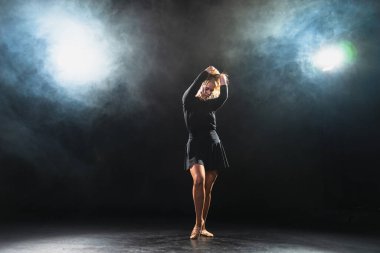 Siyah arka planda dumanla poz veren çağdaş kadın dansçı. Yetişkin kadın sanatçı ifade ile dans ediyor. Modern balerin karanlıkta dans ediyor. Tutku karanlıkta dans eder. Esneklik dengesi