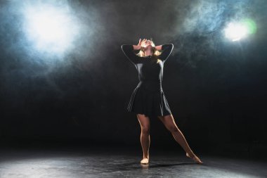 Siyah arka planda dumanla poz veren çağdaş kadın dansçı. Yetişkin kadın sanatçı ifade ile dans ediyor. Modern balerin karanlıkta dans ediyor. Tutku karanlıkta dans eder. Esneklik dengesi