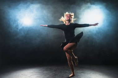 Siyah arka planda dumanla poz veren çağdaş kadın dansçı. Yetişkin kadın sanatçı ifade ile dans ediyor. Modern balerin karanlıkta dans ediyor. Tutku karanlıkta dans eder. Esneklik dengesi