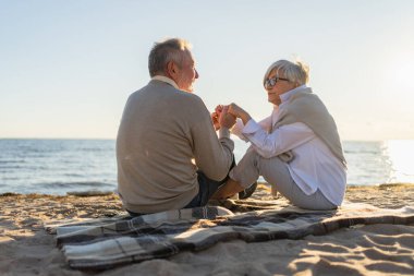 Sahilde oturmuş el ele tutuşan olgun bir çift dışarıda eğleniyor. Yaşlı karı şefkatle el ele tutuşuyor. Büyükannem ve büyükbabam birlikte. Aile âşkı