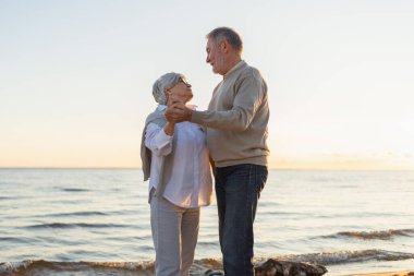 Yürümeye devam. Romantik olgun çift plaj gezisinde birlikte dans ediyor. Mutlu gülümseyen aile emeklisi kadın koca eş birlikte eğleniyor. Aile zamanı aşk bakımı