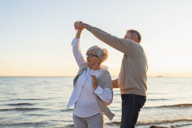 Yürümeye devam. Romantik olgun çift plaj gezisinde birlikte dans ediyor. Mutlu gülümseyen aile emeklisi kadın koca eş birlikte eğleniyor. Aile zamanı aşk bakımı