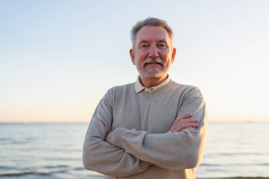 Sahilde kendine güveni tam orta yaşlı bir Avrupalı 'nın açık hava portresi. Yaşlı, olgun bir adam gülümsüyor. Mutlu büyükbaba kameraya bakıyor. Yüz portresi yakın çekim. Mutlu insanlar.