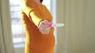 Pozitif hamilelik testi tutan kadın eli. Koca göbekli hamile bir kadın doğurganlık tedavisi görüyor ve tüp bebek bekliyor. Hamile annelik, gelecekteki annelik, ebeveynlik, yeni hayat.