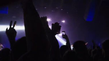 Canlı konser performansında enerjik izleyiciler. Taraftarlar el çırpıyor yaz festivalinde müzik dinliyorlar. Sahne ışıkları, heyecanlı kalabalık. Kalabalık konser salonu ve siluetleri el sallıyor.