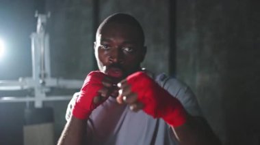 Beden eğitiminde. Afrikalı dövüşçü boksörlere yumruk atmaya hazır koruyucu bandajları kameraya sarar. Güçlü bir adam boks antrenmanına hazırlanıyor.